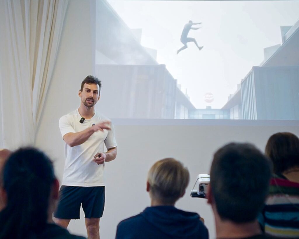 Benni Grams giving a talk in front of the screen, audience in the foreground